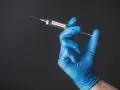 Ręka w niebieskiej rękawiczce trzyma strzykawkę z napisem "VACCINE". To symbol nadziei na bezpieczne podróże, np. do Tunezji, gdzie tunezja szczepienia są kluczowe.