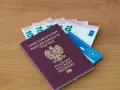 Polski paszport, euro i karta ubezpieczenia zdrowotnego na drewnianym tle.