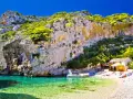 Piękna plaża z krystalicznie czystą wodą i łodzią. Ludzie odpoczywają na kamienistej plaży. Czy Chorwacja jest bezpieczna? Tak, to idealne miejsce na wakacje.