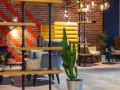 Nowoczesne wnętrze lobby hotelu Radisson Hotel Poznań Park Inn: ceglana ściana, żółte i szare fotele, regały z dekoracjami i kaktus.