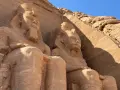 Gigantyczne kamienne posągi faraonów w Abu Simbel, Egipt, na tle skalnej ściany i błękitnego nieba.