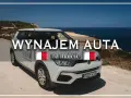 Biały samochód z napisem "Wynajem auta na Malcie" stoi na tle morza. Idealny do zwiedzania wyspy.