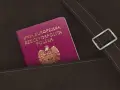 Nowy polski paszport w kolorze fuksji z godłem orła w złocie, schowany w brązowej skórzanej kieszeni.