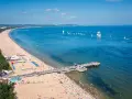 Słoneczna plaża z molo, tłumy ludzi i żaglówki na morzu – idealne miejsce na tanie wycieczki z Gdańska.