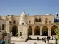 Ludzie spacerują po dziedzińcu z kamiennymi budynkami i kopułą. Czy w Izraelu jest bezpiecznie? Turyści zwiedzają historyczne miejsca.