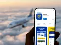 Ręka trzyma smartfon z aplikacją Ryanair, gotową do odprawy online. W tle leci samolot.
