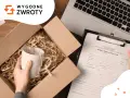 Ręka wkłada kubek do kartonu, obok formularz zamówienia i laptop. To ułatwia tui reklamacje.