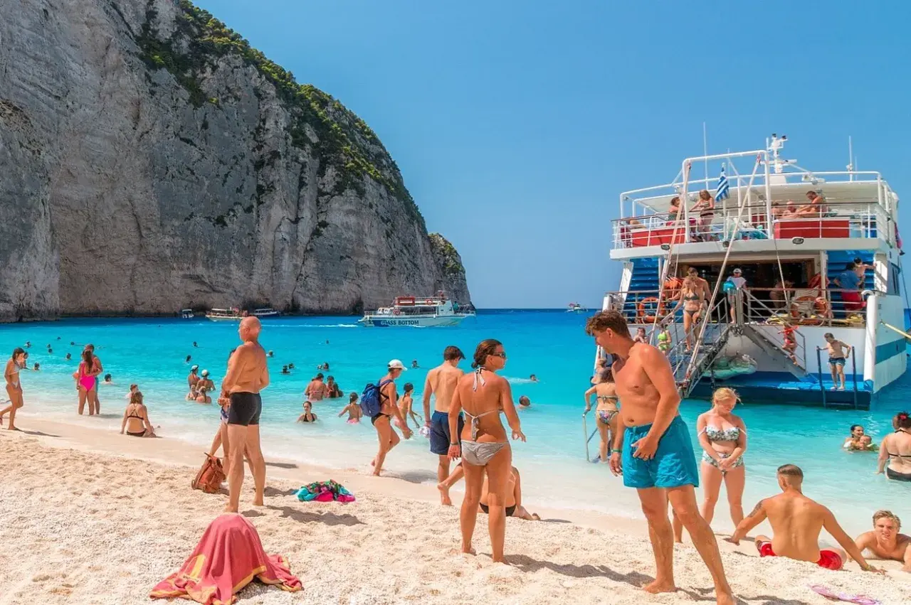 Tui promocje na wakacje: ludzie na plaży Navagio, Zakynthos, Grecja. Turkusowa woda, biały piasek i klify.