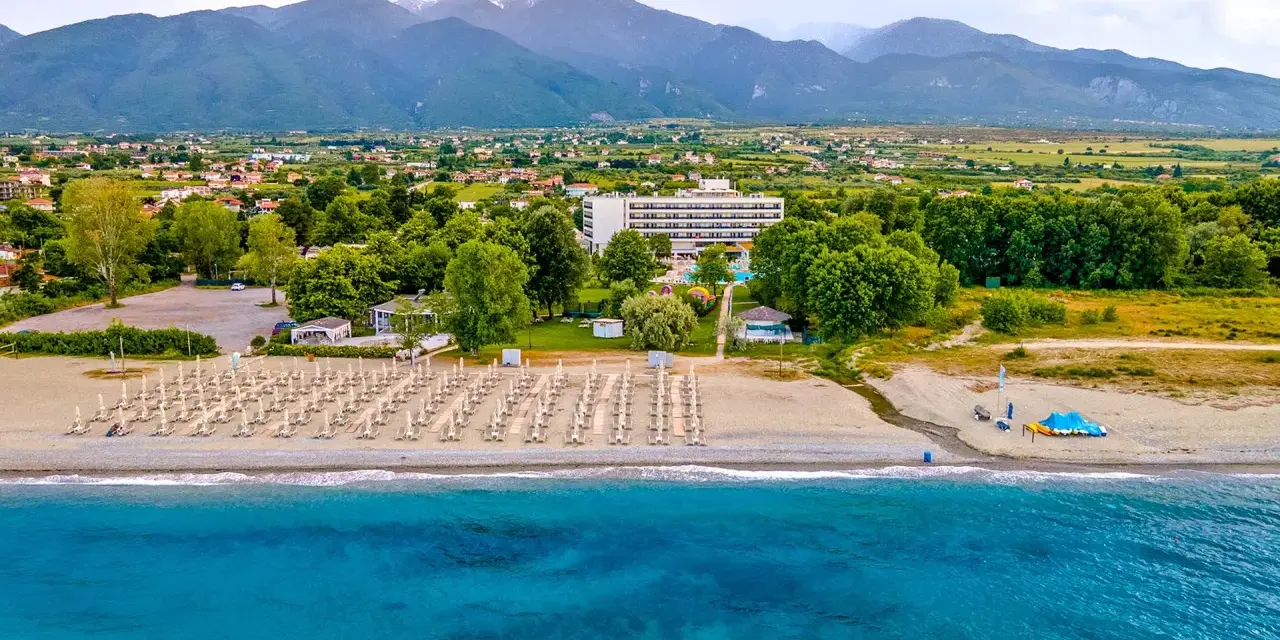 Piękna plaża na Riwierze Olimpijskiej z rzędami leżaków, hotelem i górami w tle.