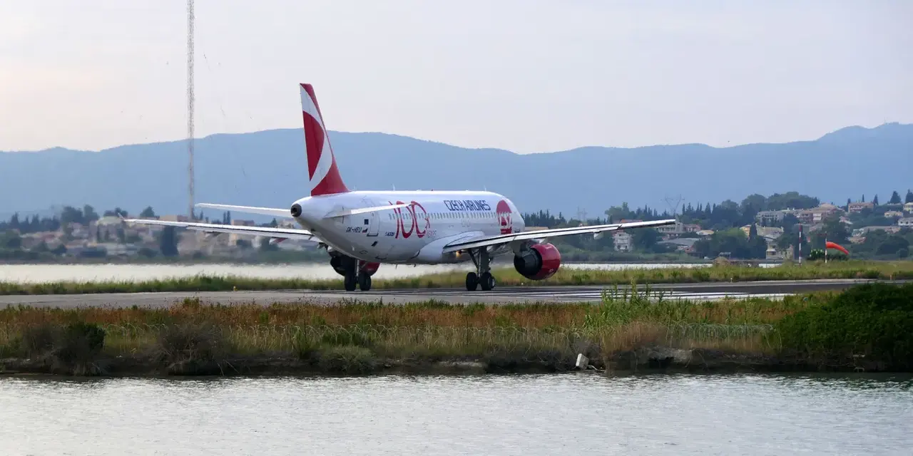 Samolot Czech Airlines na pasie startowym lotniska na Korfu, z wodą i zielenią w tle.