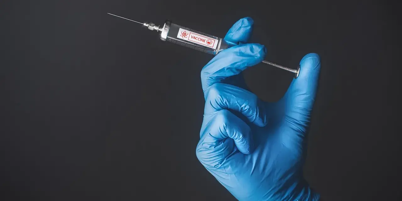 Ręka w niebieskiej rękawiczce trzyma strzykawkę z napisem "VACCINE". To symbol nadziei na bezpieczne podróże, np. do Tunezji, gdzie tunezja szczepienia są kluczowe.