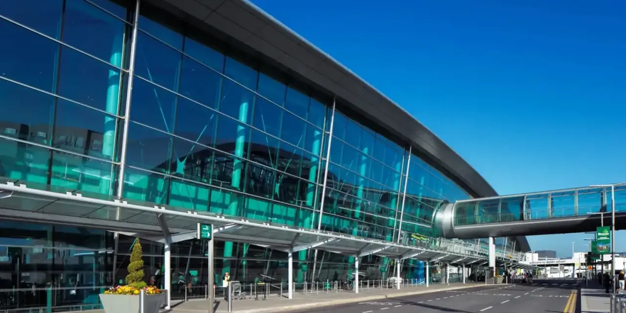 Nowoczesny budynek z przeszkloną fasadą, widoczny jest pas startowy i kładka dla pieszych. To wejście na dublin lotnisko.