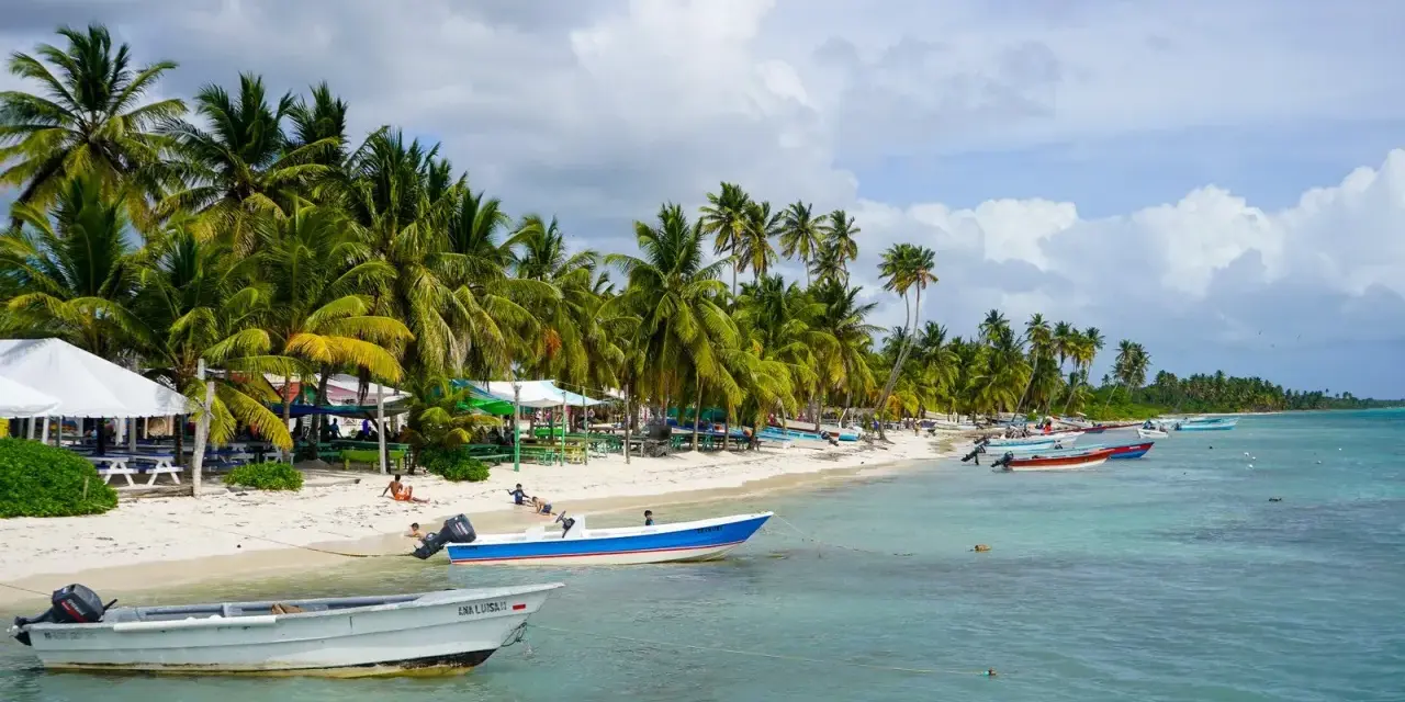 Rajski **Bavaro Beach** z palmami, białym piaskiem, turkusową wodą i łodziami.
