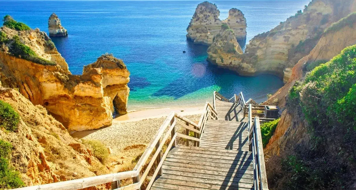 Schody prowadzą na piaszczystą plażę z turkusową wodą i skalnymi formacjami. Idealne miejsce na portugalia wakacje.