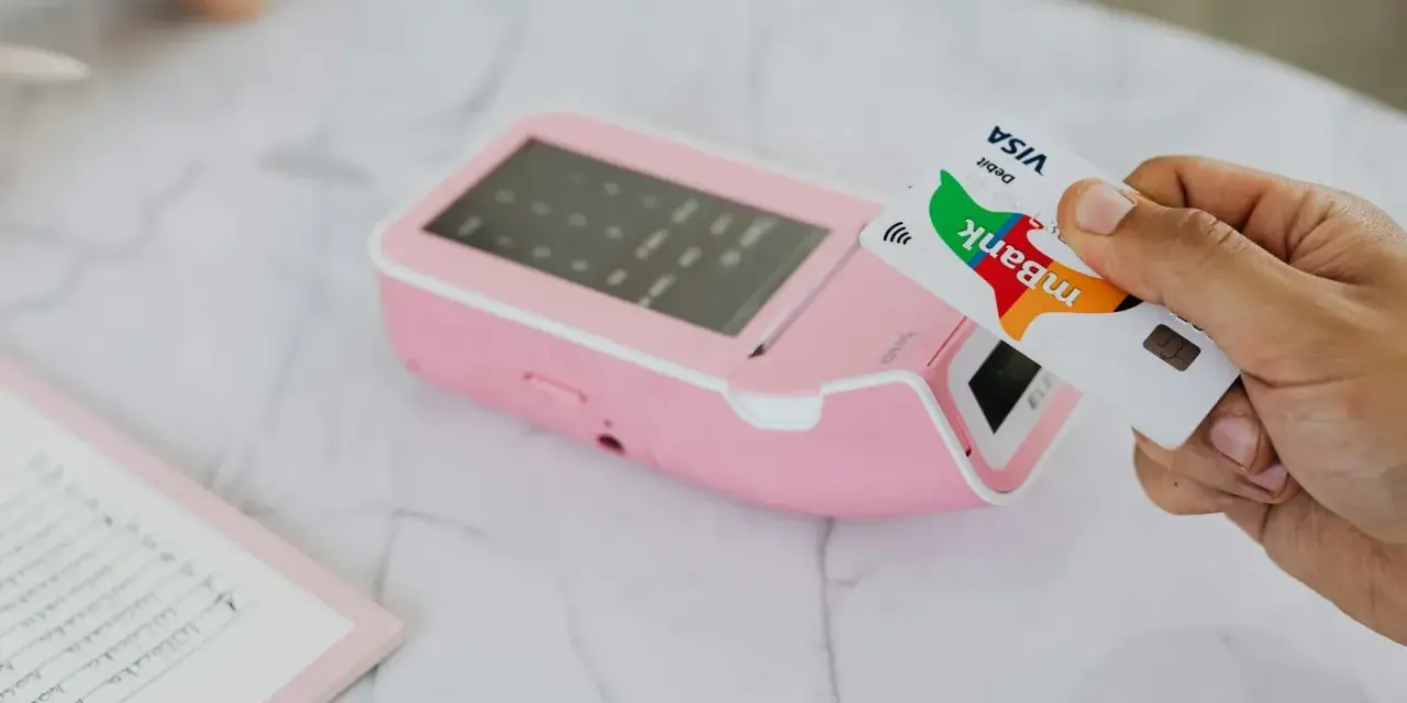 Zbliżenie na kartę Visa mBank zbliżającą się do terminala płatniczego. Płatność zbliżeniowa, wygodna waluta w Czechach.
