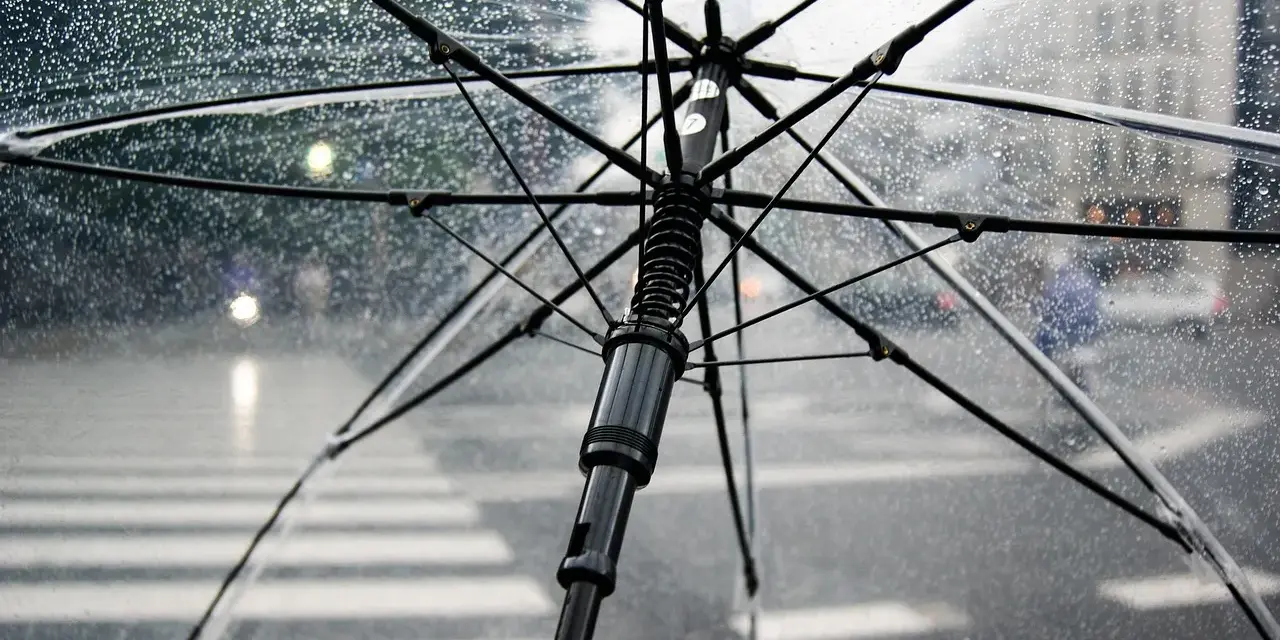 Przezroczysty parasol w bagażu podręcznym chroni przed deszczem na ulicy. Krople wody na materiale.