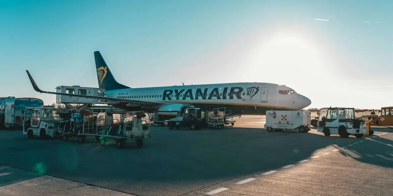 Samolot Ryanair na płycie lotniska, w tle widać wózki z bagażem rejestrowanym.