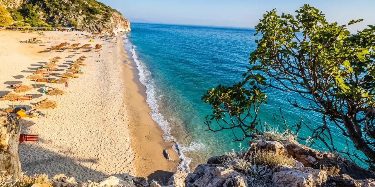 Piękna plaża w Albanii, gdzie ceny są przystępne. Słoneczny dzień, turkusowa woda i zielone wzgórza.