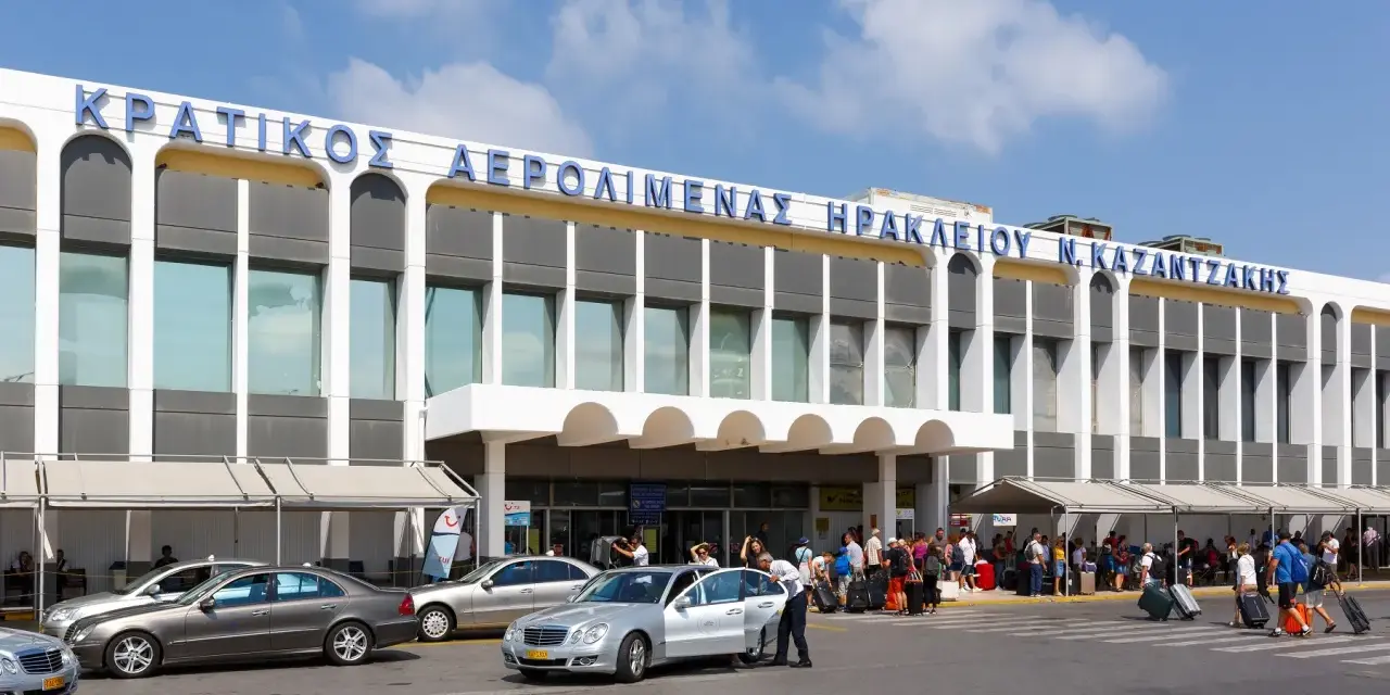 Lotnisko na Krecie, Heraklion N. Kazantzakis. Ludzie z bagażami czekają na transport przed nowoczesnym budynkiem terminalu.