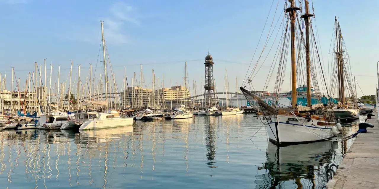 Port w Barcelonie, pełen żaglówek i statków, z wieżą widokową w tle. Czy w Barcelonie jest bezpiecznie? Tak, to spokojne miejsce.
