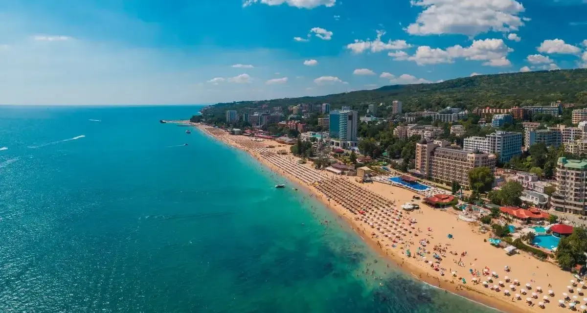 Słoneczne Złote Piaski wakacje: szeroka plaża z leżakami, turkusowe morze i hotele w tle. Idealne miejsce na relaks.
