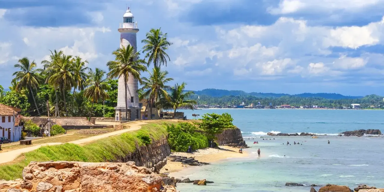 Latarnia morska na Sri Lance, otoczona palmami, z widokiem na ocean i plażę. Idealne miejsce na wakacje, warto sprawdzić wizę Sri Lanka.