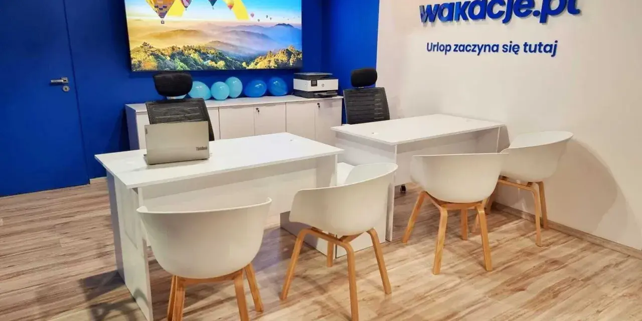 Nowoczesne biuro z logo "wakacje.pl", ekranem z balonami i białymi biurkami.