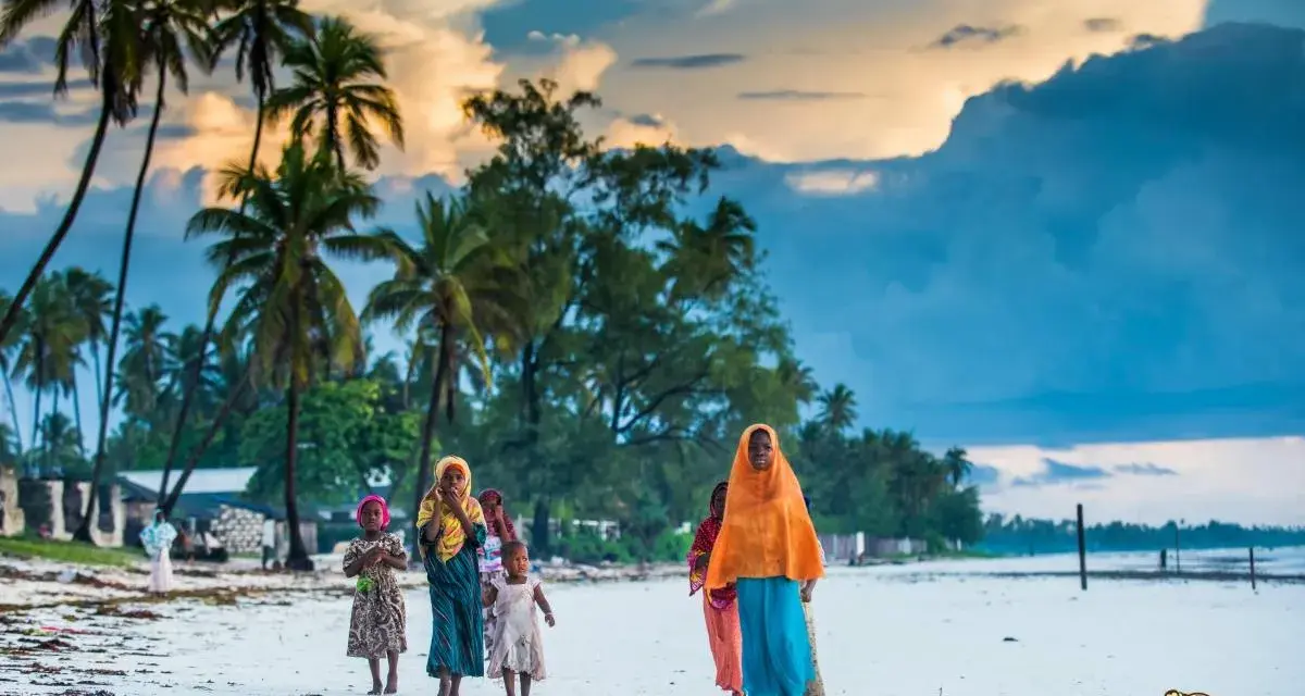 Dzieci na plaży podczas wycieczki na Zanzibar. Palmy i chmury tworzą tło dla tej sceny.