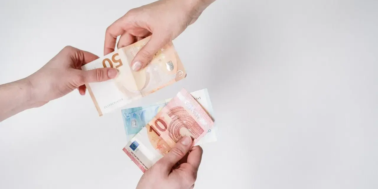 Dwie dłonie przekazują sobie banknoty euro. W Hiszpanii obowiązuje euro, więc to właśnie ta waluta jest tu widoczna.