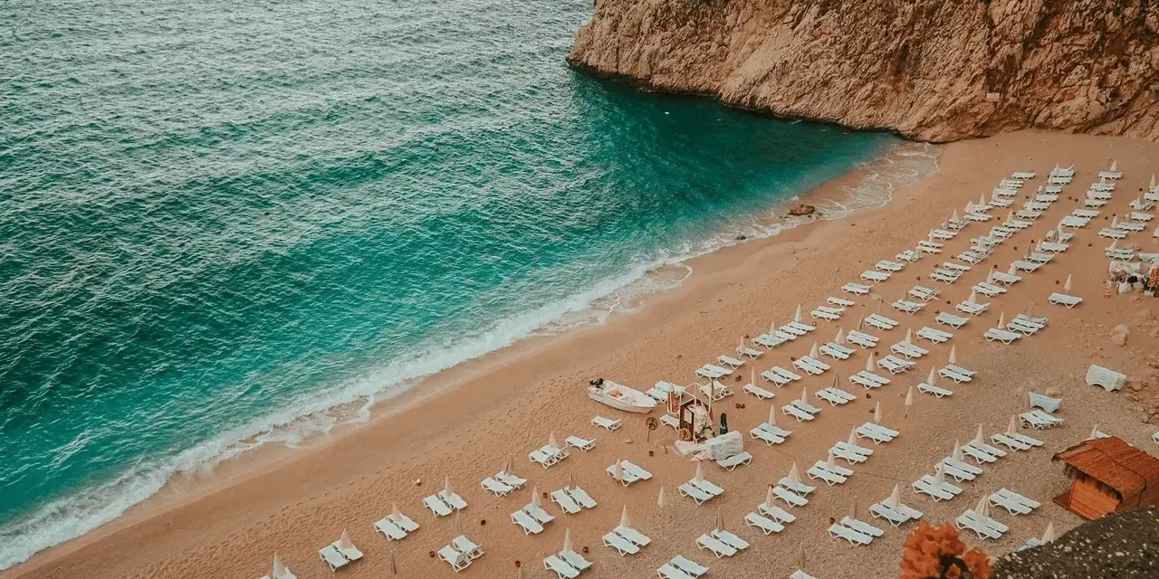 Piękna plaża w Turcji, turkusowe morze obmywa piaszczysty brzeg, a rzędy leżaków czekają na turystów.
