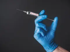 Ręka w niebieskiej rękawiczce trzyma strzykawkę z napisem "VACCINE". To symbol nadziei na bezpieczne podróże, np. do Tunezji, gdzie tunezja szczepienia są kluczowe.