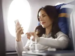Kobieta korzysta z telefonu, ciesząc się **wifi w samolocie** podczas lotu.
