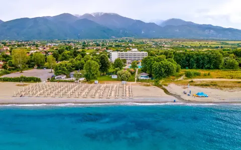 Piękna plaża na Riwierze Olimpijskiej z rzędami leżaków, hotelem i górami w tle.