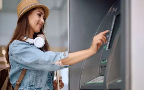 Kobieta w słomkowym kapeluszu i dżinsowej kurtce korzysta z bankomatu.