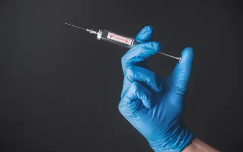 Ręka w niebieskiej rękawiczce trzyma strzykawkę z napisem "VACCINE". To symbol nadziei na bezpieczne podróże, np. do Tunezji, gdzie tunezja szczepienia są kluczowe.