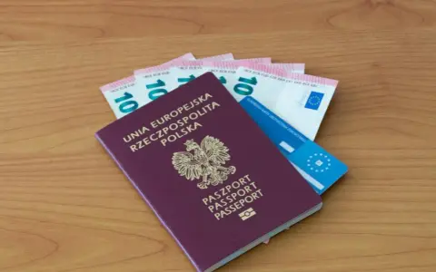 Polski paszport, euro i karta ubezpieczenia zdrowotnego na drewnianym tle.