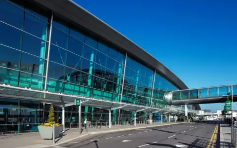 Nowoczesny budynek z przeszkloną fasadą, widoczny jest pas startowy i kładka dla pieszych. To wejście na dublin lotnisko.