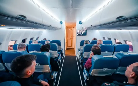 Wnętrze samolotu z pasażerami siedzącymi w rzędach. Wiele osób podróżuje, co potwierdza, że to najbezpieczniejszy środek transportu.