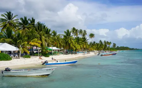 Rajski **Bavaro Beach** z palmami, białym piaskiem, turkusową wodą i łodziami.