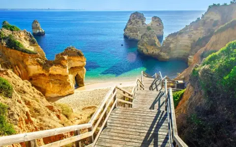 Schody prowadzą na piaszczystą plażę z turkusową wodą i skalnymi formacjami. Idealne miejsce na portugalia wakacje.