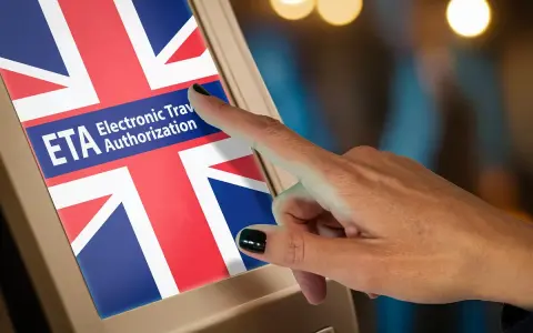 Dłoń dotyka ekranu z flagą Wielkiej Brytanii i napisem "ETA Electronic Travel Authorization".