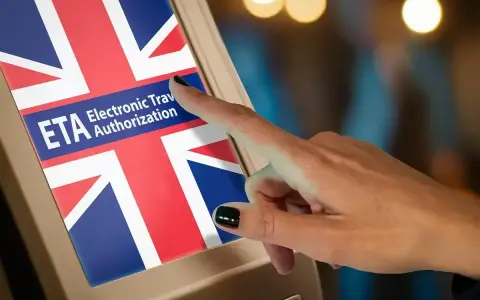 Dłoń dotyka ekranu z flagą Wielkiej Brytanii i napisem "ETA Electronic Travel Authorization". Czy do Londynu trzeba paszport? Sprawdź ETA.