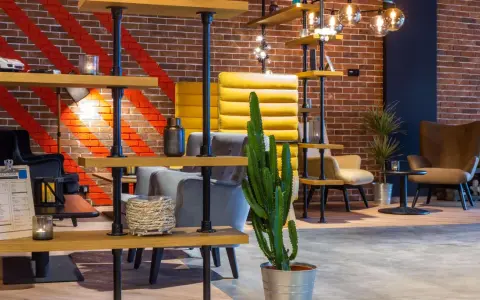Nowoczesne wnętrze lobby hotelu Radisson Hotel Poznań Park Inn: ceglana ściana, żółte i szare fotele, regały z dekoracjami i kaktus.