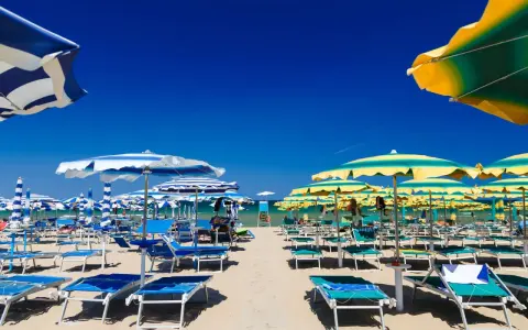Słoneczna plaża we Włoszech z rzędami leżaków i parasoli. Marzysz o tanich lotach do Włoch z Warszawy?