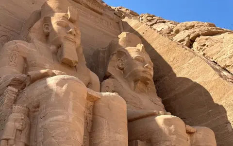 Gigantyczne kamienne posągi faraonów w Abu Simbel, Egipt, na tle skalnej ściany i błękitnego nieba.