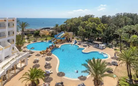 Hotel Marhaba Royal Salem kusi basenem z wodnymi zjeżdżalniami i palmami, w tle morze.