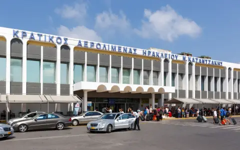 Lotnisko na Krecie, Heraklion N. Kazantzakis. Ludzie z bagażami czekają na transport przed nowoczesnym budynkiem terminalu.