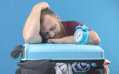 Zmęczony podróżnik śpi na walizce obok budzika. Czy to jetlag?