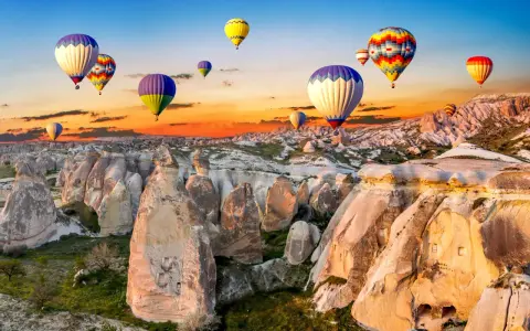 Kolorowe balony unoszą się nad skalistym krajobrazem Kapadocji o wschodzie słońca. Idealne miejsce na wakacje all inclusive!