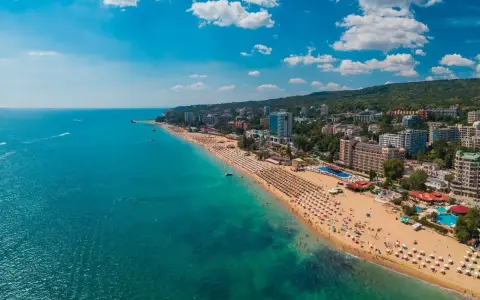 Słoneczne Złote Piaski wakacje: szeroka plaża z leżakami, turkusowe morze i hotele w tle. Idealne miejsce na relaks.